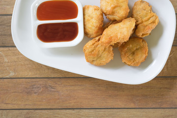 chicken nuggets putting in dish. have small cup with chilli sauce and tomato sauce all of it putting on wooden table are background. this image for food concept
