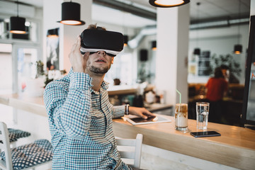 Fototapeta premium Young handsome man sitting in cyber cafe and using virtual reality headset or glasses.