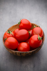 Small plum tomatoes in a wooden bowl on a gray background.