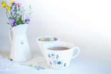 Obraz na płótnie Canvas Cup of tea with meadow's flowers in vase