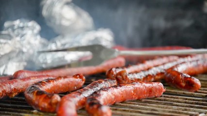 Seamless loop - Fork turning over tasty juicy sausages grilling  on a barbecue with potatoes in foil, video HD