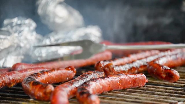 Seamless loop - Fork turning over tasty juicy sausages grilling  on a barbecue with potatoes in foil, video HD