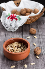 Vertical capture of pumpkin seeds in earthenware pot and walnuts in basket on wooden table
