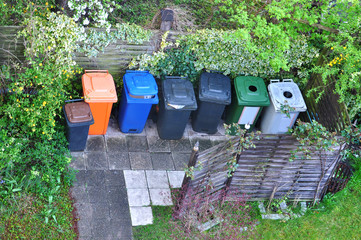 Many plastic containers for separate garbage among the greenery. Top view.