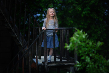 A nice little girl is standing on an antique antique staircase in a village on a summer evening