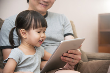 Asian kid and her father sitting and using digital tablet together.