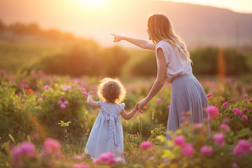 Beautiful child girl with young mother are wearing casual clothes walking in roses garden over...