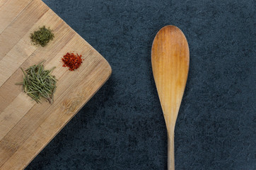 Spices such as dried rosemary plants, dills and red pepper on wooden chopping board with spoon on...