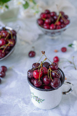 Close up Fresh cherry fruit in white mug, other dishes with berries and vase with jasmine flowers on the light marble table. Soft selective focus. Summer countryside concept