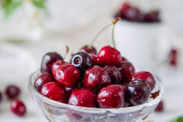 Close up Fresh cherry fruit in glass vase, other dishes with berries and jar with jasmine and wildflowers on the light marble table. Soft selective focus. Summer countryside concept