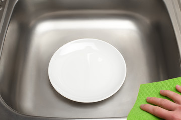 Kitchen sink with clean plate and green rag in hand