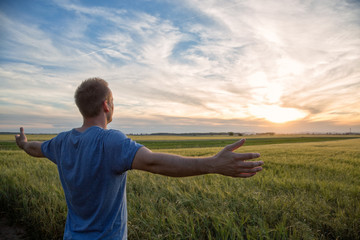 Man standing in an open field at sunset with open arms - embracing nature - obrazy, fototapety, plakaty