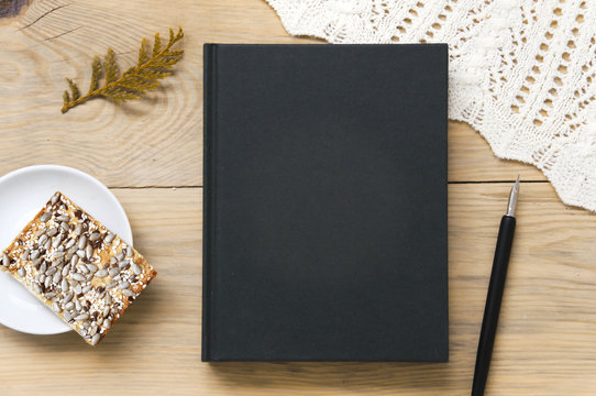 Mock up of black book on a wooden background with a pen and cookies with seeds. Top view.
