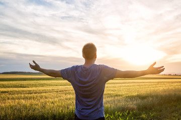 Man standing in an open field at sunset with open arms - embracing nature