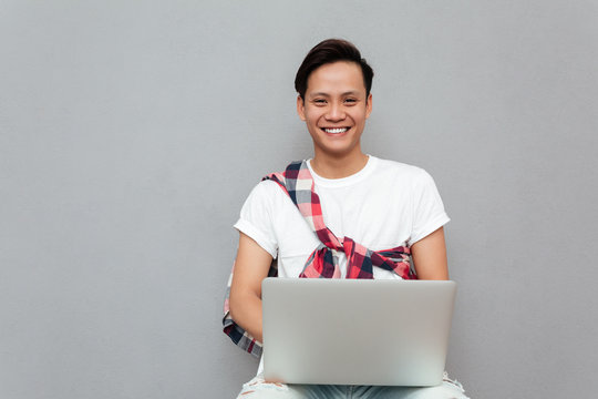 Happy Young Asian Man Over Grey Background Using Laptop