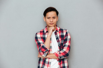 Serious asian man standing over grey wall.