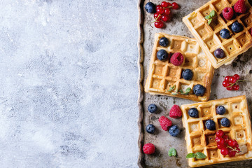 Homemade square belgian waffles with fresh ripe berries blueberry, raspberry, red currant on vintage metal tray over gray texture background. Top view with space