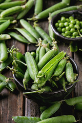 Young organic green pea pods and peas in bowls over old dark wooden planks background. Close up. Harvest, healthy eating.