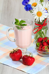 Glass of yogurt  with mint and fresh strawberries, chamomile and cornflowers in vase on the table