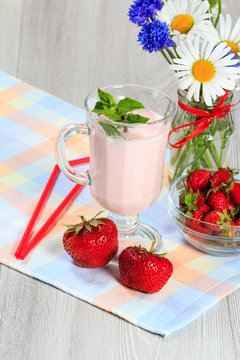 Glass of yogurt  with mint and fresh strawberries, chamomile and cornflowers in vase on the table