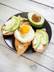 Delicious breakfast. Sandwiches with avocado and egg on a dark plate on wooden background. Flat lay. Top view.