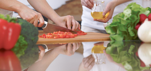 Close-up of four human hands are cooking in a kitchen. Friends having fun while preparing fresh...