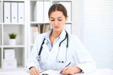 Young brunette female doctor sitting at the table and working at hospital office.  