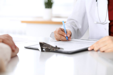 Close up of a female doctor filling up  an application form while consulting patient