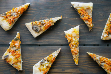Pattern of triangular pieces of pizza on a dark wooden table top view.