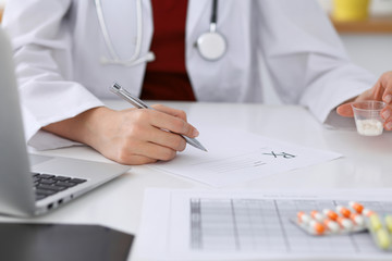 Female medicine doctor fills up  prescription form to patient closeup. Panacea and life save,...