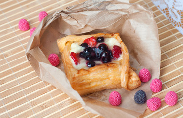 Pastry with red berries on paper, isolated on a wooden background. Summer fruit dessert.