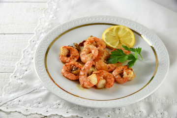 fried tiger prawns, marinated with garlic, spices, herbs and lemon on a fine white plate, italian parsley garnish, copy space on the bright background