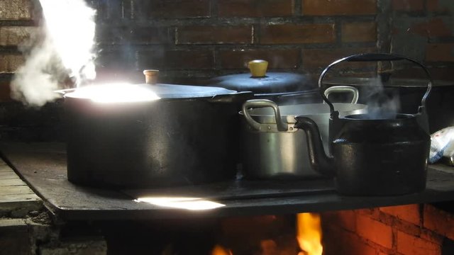 4k close up of the rustic Brazilian farmhouse wood burning stove. Large pans on large open fronted iron wood burning stove with the chef lifting the lids and stirring and checking the food.