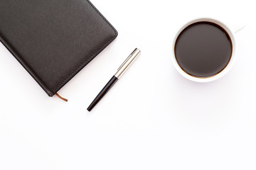 Cup of black coffee and a black day planner with pen on white background. Minimal business concept.