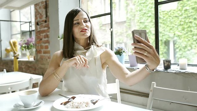 Elegant woman sitting in the cafe and doing selfies on smartphone, steadycam shot
