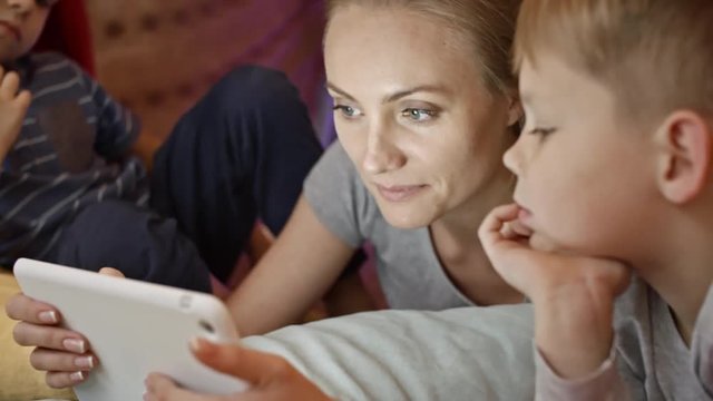 Closeup of mother lying on floor, using digital tablet and telling something to little sons