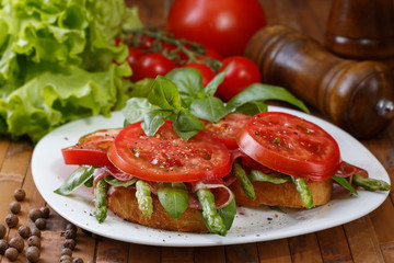 Two toast with asparagus, ham, tomato  and basil on a white plate, close-up.