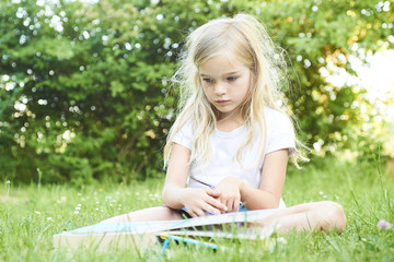Cute child girl reading book in summer garden outdoor. Kids learning on summer vacations. Messed hair from the wind. 