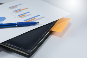 Fototapeta premium Notebook close-up. Notebook with a pencil on a white background. White piece of paper and charts with blue pen on white background.