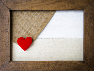 Red heart on canvas and hessian fabric texture in vintage wooden frame