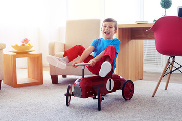 Cheerful small boy sitting on red retro toy car