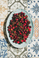 Fresh ripe sweet cherries in blue plate over colorful oriental ceramic tiles background, top view, flat lay. Summer food concept