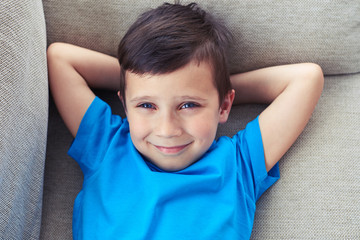 Small boy holding hands behind head lying on the sofa