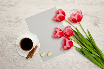 Fototapeta na wymiar Pink tulips on a blank sheet of paper, mug of coffee and marshmallows, light wooden background. top view, space for text