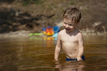 A little boy stands in the water of the lake to the waist and smiling