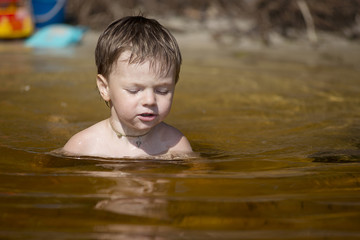 little boy learning to swim in the lake on a Sunny day