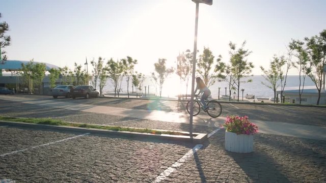 Young stylish woman cyclist enjoying fixed gear bike riding outdoors at sunrise near the sea