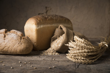 Bread border on wood with copy space background. Brown and white whole grain loaves still life composition with wheat ears scattered around. Bakery and grocery food store concept.