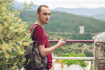 Man traveler with backpack looking at his smartphone on the background of nature and the mountains