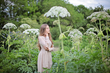 Young attractive teenager girl in vintage dress dream and walk park surraunded by high flowers of Heracleum or hogweed. Magic fairy childhood scene. Simple life, ecology style fashion clothes concept